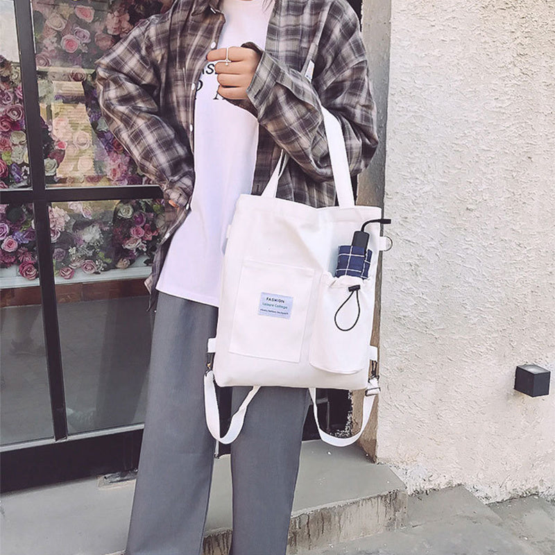 Stylish student holding a white canvas handbag with pockets, wearing plaid shirt and casual clothes, showcasing a trendy look.