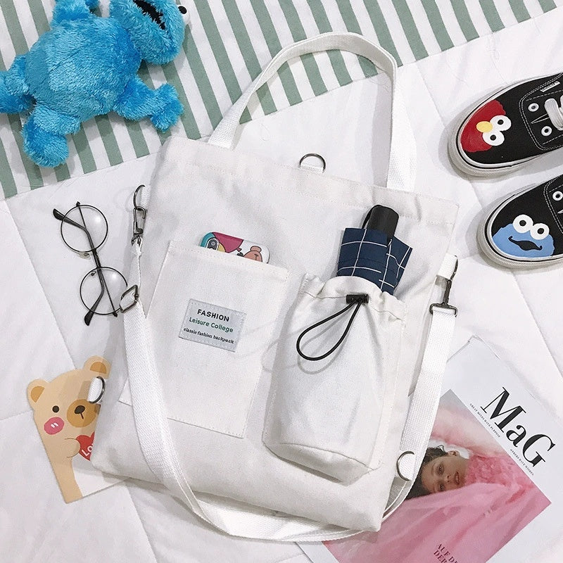 White canvas handbag with pockets, umbrella, glasses, and cute plush toys on striped surface.