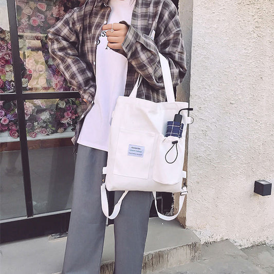 Stylish student holding a white canvas handbag with pockets, wearing plaid shirt and casual clothes, showcasing a trendy look.